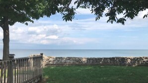 A grassy area with a stone wall and a wooden fence, leading to a body of water.