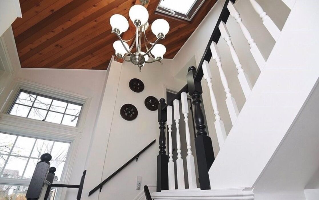 A staircase with white balusters and black handrails, a wooden ceiling, and a chandelier.