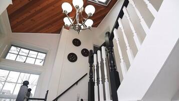 A staircase with white balusters and black handrails, a wooden ceiling, and a chandelier.