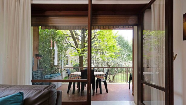 Een kamer met een schuifglazen deur die uitkomt op een terras buiten, met een tafel en stoelen.