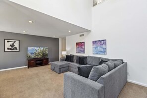 A living room with a sectional sofa, a flat-screen TV, and artwork on the walls.