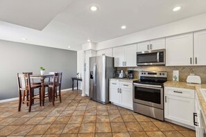 A modern kitchen with white cabinets, stainless steel appliances, and a dining area with wooden chairs.