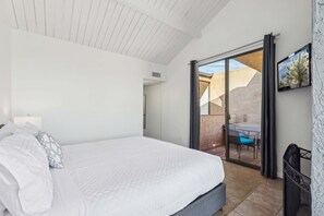 A bedroom with a bed, a nightstand, a lamp, a sliding glass door leading to an outdoor patio with a table and chairs.
