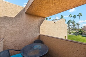 A balcony with a table and chairs, a view of palm trees, and a building with a textured facade.
