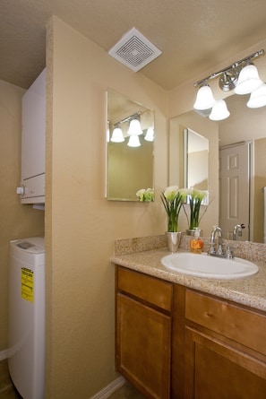 Un baño con lavabo, espejo y electrodoméstico blanco.