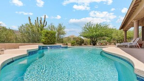 Ein klares Schwimmbecken mit gefliestem Rand, umgeben von einer Terrassenanlage mit Liegestühlen und einer Pergola.