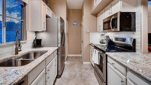 A narrow kitchen with stainless steel appliances, white cabinets, and a window with a view. - Harmony Haven! Your Artful Escape (Scottsdale)