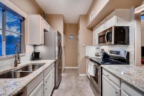 A narrow kitchen with stainless steel appliances, white cabinets, and a window with a view.