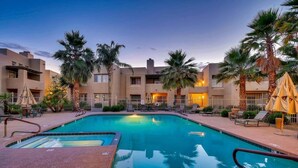 A swimming pool with lounge chairs and umbrellas, surrounded by palm trees and a building with balconies. - Harmony Haven! Your Artful Escape (Scottsdale)