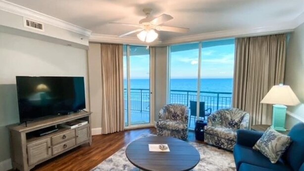 Quarto com televisão, mesa de centro redonda, duas poltronas estampadas, um sofá e vista para o oceano.