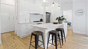 A modern kitchen with white cabinetry, a central island with stools, pendant lighting, and a visible clock on the wall. - Sierra Cottage (East Toowoomba)