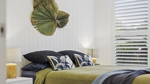 A bedroom with a bed, two nightstands, a wall-mounted decorative leaf, and a window with blinds. - Sierra Cottage (East Toowoomba)