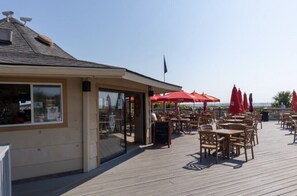 Un espace extérieur aménagé pour les repas, avec des parasols rouges, des tables et des chaises en bois.
