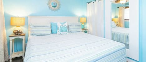 A bedroom with a large bed, two bedside tables with lamps, a ceiling fan, and a mirror on the wall.