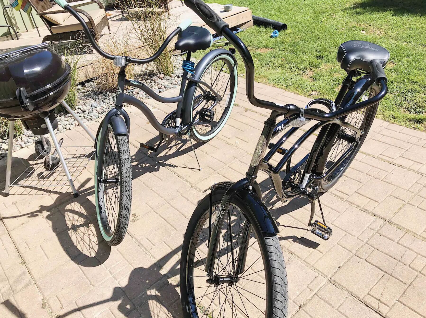 A bicycle parked on a paved patio with a grill and outdoor furniture in the background.