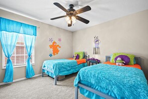 A bedroom with two beds, a ceiling fan, and a window with blue curtains.