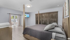 A bedroom with a bed, a wooden headboard, a television, and a window with blinds. - Downtown Retreat (Fort Myers)