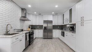A modern kitchen with white cabinetry, a stainless steel refrigerator, and a wooden floor. - Downtown Retreat (Fort Myers)
