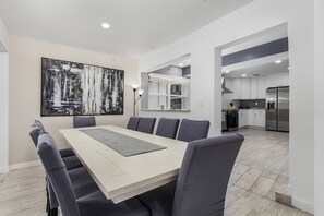 Uma área de jantar moderna com uma mesa grande, seis cadeiras e uma pintura contemporânea na parede.
