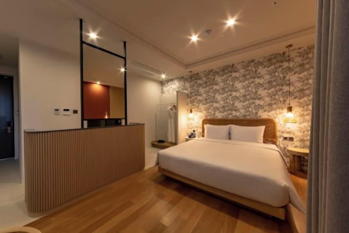 Une chambre d’hôtel moderne avec un lit en bois, une table de chevet, un miroir et un mur orné d’un motif floral.
