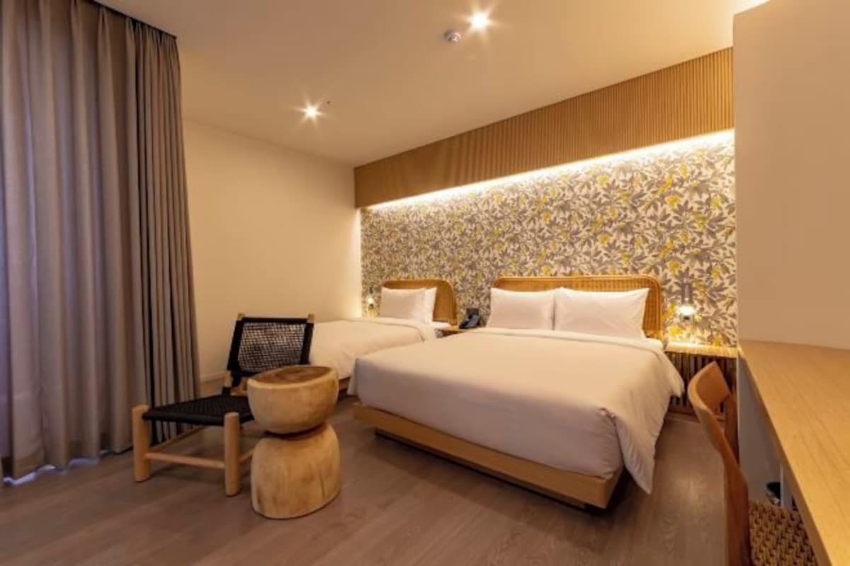 Une chambre d’hôtel moderne avec deux lits, une table de chevet en bois, une chaise et un mur décoré de motifs.