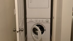 Un lavadero pequeño con lavadora y secadora de carga frontal, una puerta con picaporte plateado y un estante sobre la secadora.