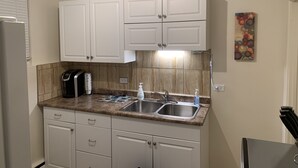 Cocina con armarios blancos, encimera de granito, pileta doble, cafetera y un cuadro colgado en la pared.