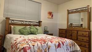 Un dormitorio con cabecera de cama de madera, ropa de cama verde y blanca, un aparador de madera y un espejo.