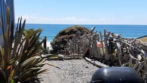 Ein gepflasterter Weg führt zu einem Strand, auf dem sich ein großes schwarzes Objekt und ein kleines orangefarbenes Objekt befinden.