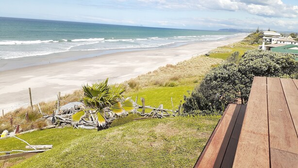 Blick auf einen Strand mit einer Holzterrasse, Rasenflächen und einer fernen Küstenlinie.