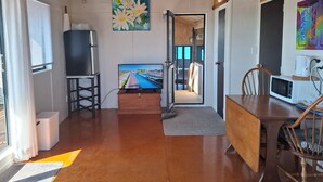 A modern living room with a wooden ceiling, a flat-screen TV, a dining table with chairs, and a painting on the wall. - Pukehina Beach Studio with Balcony and Majestic views (Te Puke)