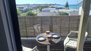 Ein Balkon mit Tisch und Stühlen, der auf eine Küstenlandschaft mit Gebäuden und Meerblick blickt.