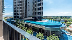 A modern hotel with a large infinity pool, high-rise buildings in the background, and a view of the surrounding landscape. - 3BR Homestay with Pool View Bukit Rimau (Shah Alam)
