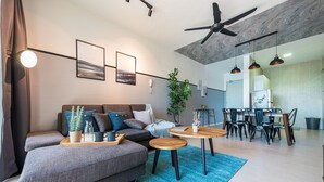 A modern living room with a sofa, coffee table, and dining area. - 3BR Homestay with Pool View Bukit Rimau (Shah Alam)