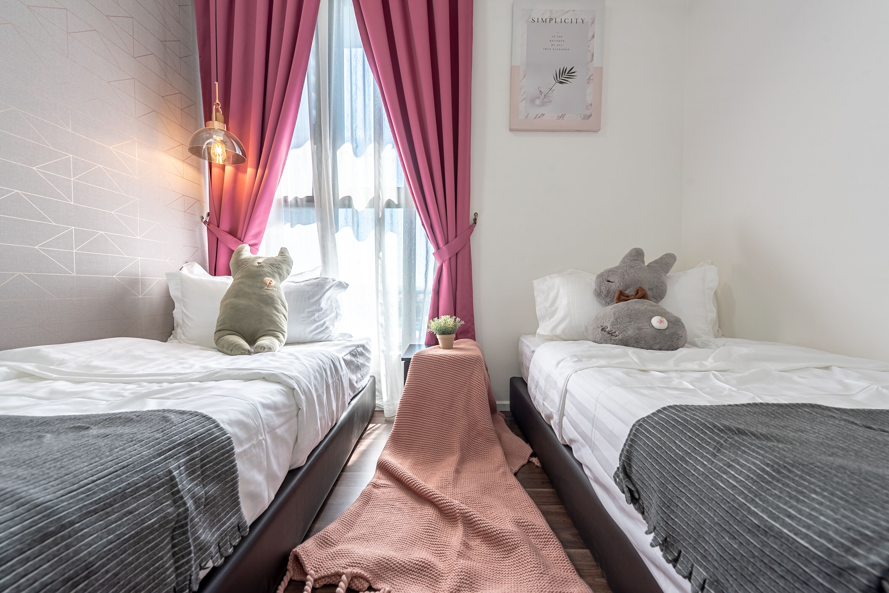 A bedroom with two beds, a pink curtain, a small table with a plant, and a wall with a geometric pattern.