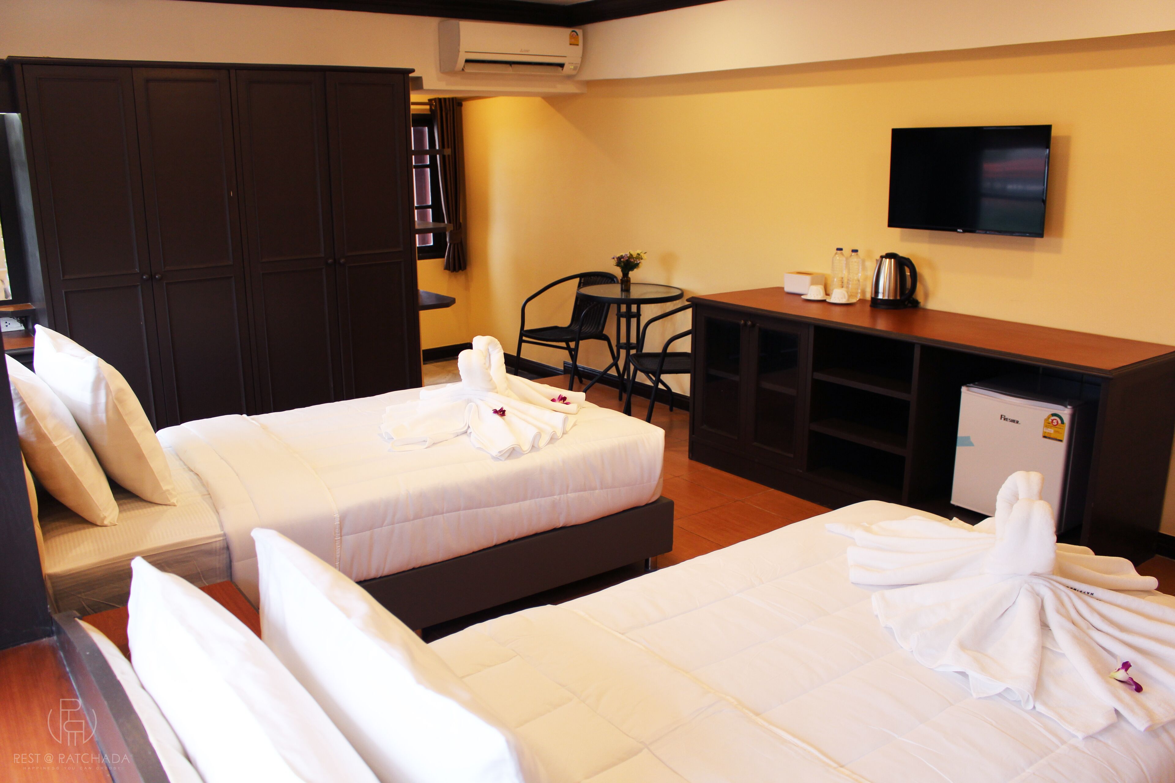 A hotel room with two beds, a desk, a TV, and a minibar.