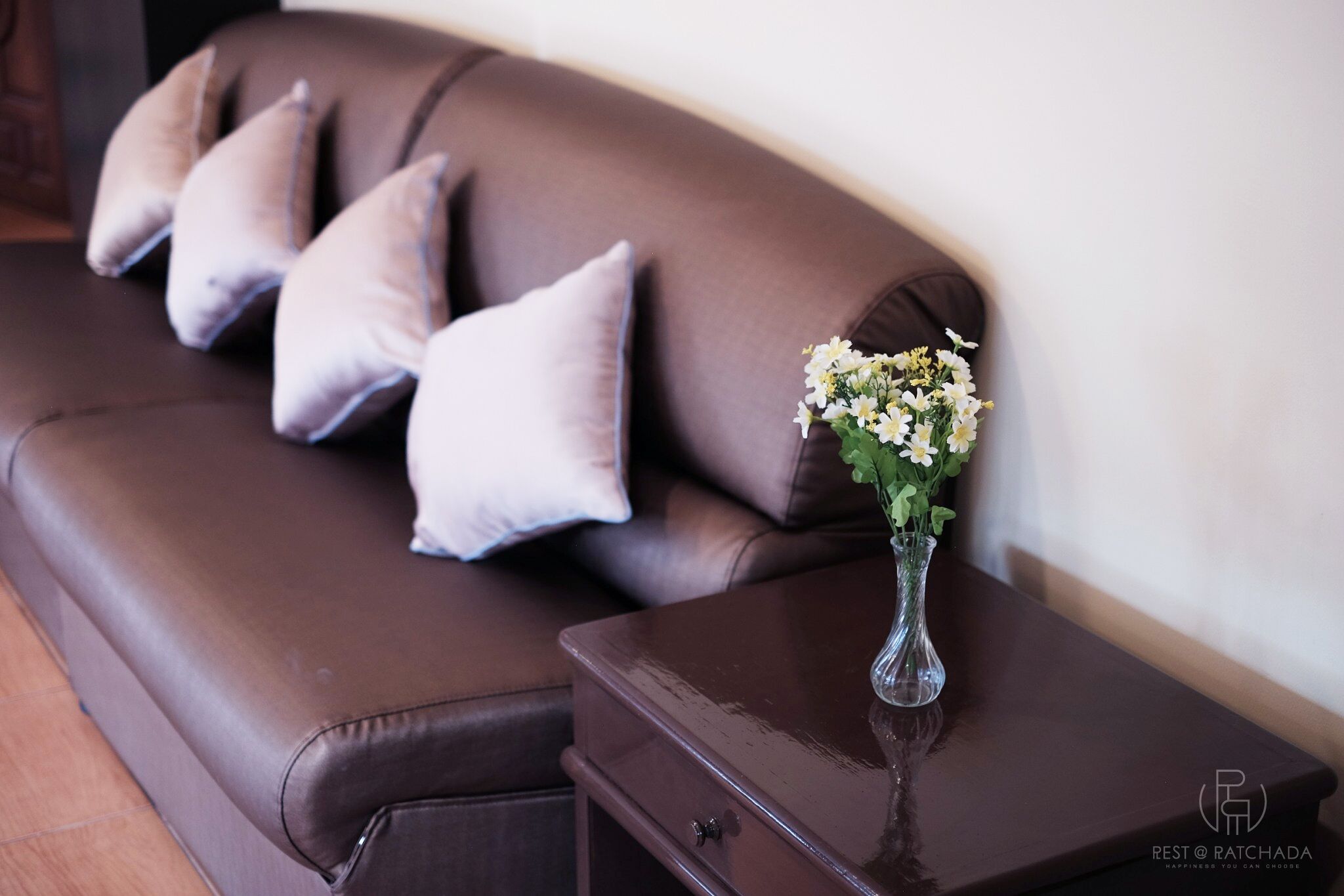 A brown leather sofa with multiple cushions and a vase with flowers on a wooden side table.