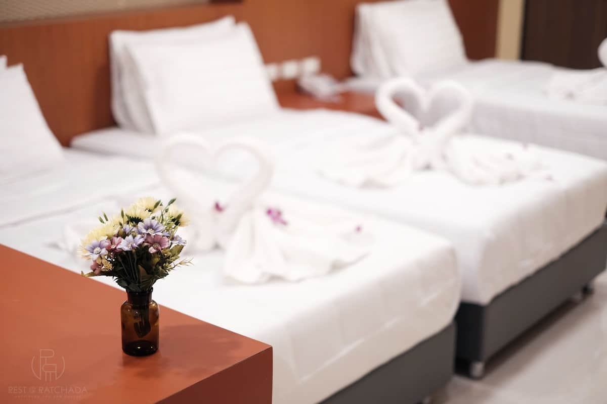 Ein Hotelzimmer mit zwei Betten, weißen Leinentüchern, herzförmigen Handtüchern und einer Blumenvase auf einem Holztisch.