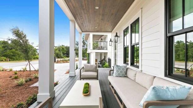 A covered porch with a wooden ceiling, white walls, and large windows. There is a seating area with a sofa and chairs, and a small table with a decorative item. - 169 Lakeview Drive (Santa Rosa Beach)