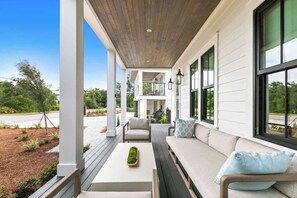 A covered porch with a wooden ceiling, white walls, and large windows. There is a seating area with a sofa and chairs, and a small table with a decorative item. - 169 Lakeview Drive (Santa Rosa Beach)