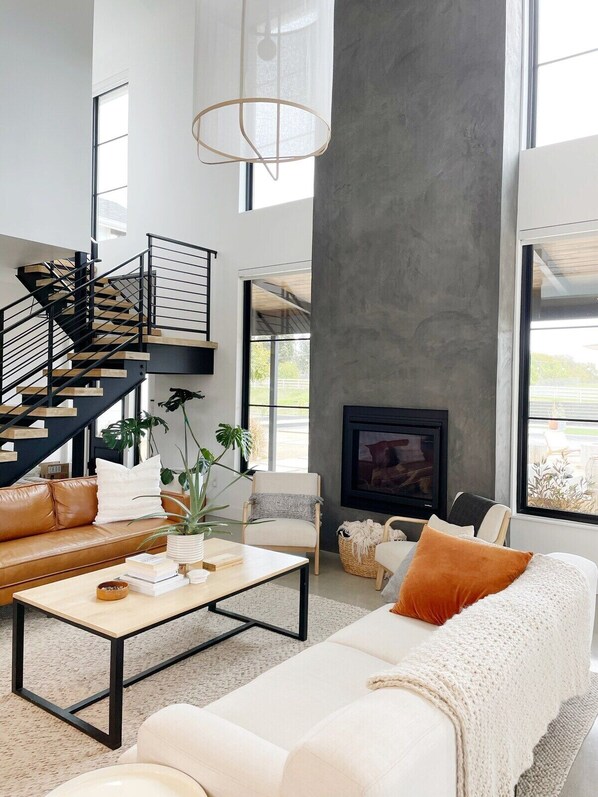A modern living room with a staircase, a fireplace, and large windows.
