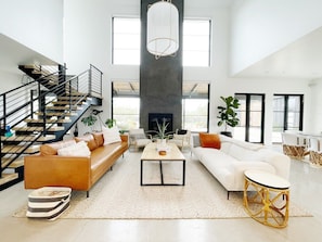 Relax in a spacious living area with high ceilings and large windows, featuring a modern staircase, leather and white sofas, and a fireplace.