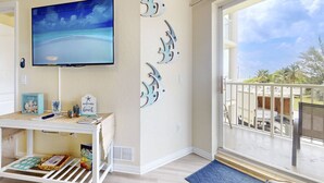 Una stanza con televisore, un tavolino con oggetti decorativi, un balcone vista spiaggia e un cartello con su scritto 'benvenuti alla spiaggia'.