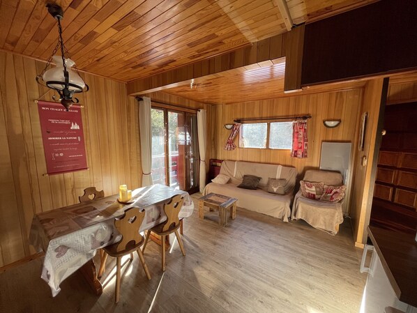 A wooden interior with a dining table, chairs, a sofa, and a ceiling fan.