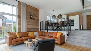 Un salon moderne avec un canapé d’angle, une table basse et un fauteuil noir. Un escalier mène à un niveau supérieur où se trouve un coin repas.