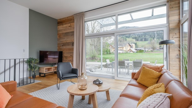 Un salon moderne avec un canap é en cuir, un téléviseur et une grande fenêtre donnant sur un jardin et des immeubles.