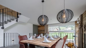 Un espace repas moderne avec une table en bois dressée pour six personnes, entourée de chaises en cuir. Deux grandes lampes suspendues en fibres tressées sont placées au-dessus de la table.