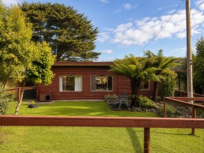 A red wooden house with a fenced yard, a small garden, and a large tree. - Top of the Otways the Country Cottage (Barramunga)
