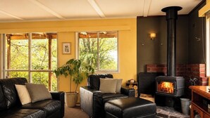 A cozy living room with a fireplace, leather sofas, and a large window. - Top of the Otways the Country Cottage (Barramunga)