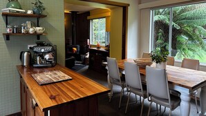 A cozy kitchen with a wood-burning stove, a coffee machine, and a dining area with chairs and a table. - Top of the Otways the Country Cottage (Barramunga)
